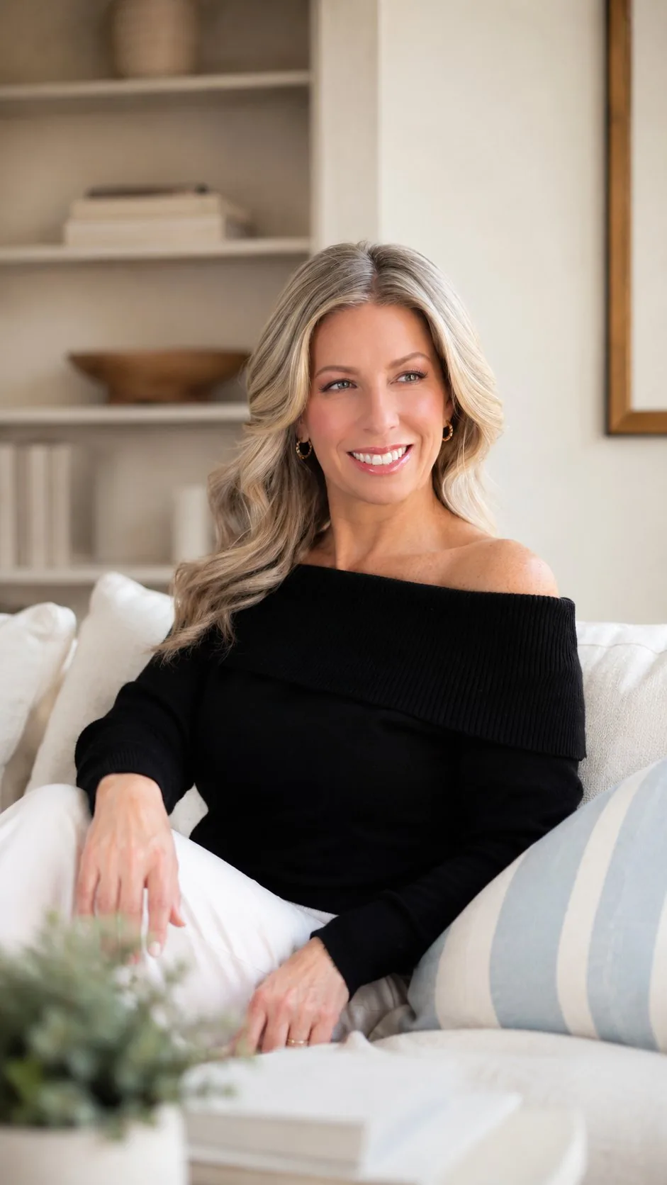 Kendal seated on a sofa in a black off-shoulder sweater